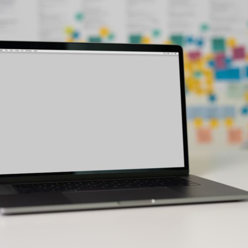 A laptop on a desk with a gray screen and colorful post-it notes in the background