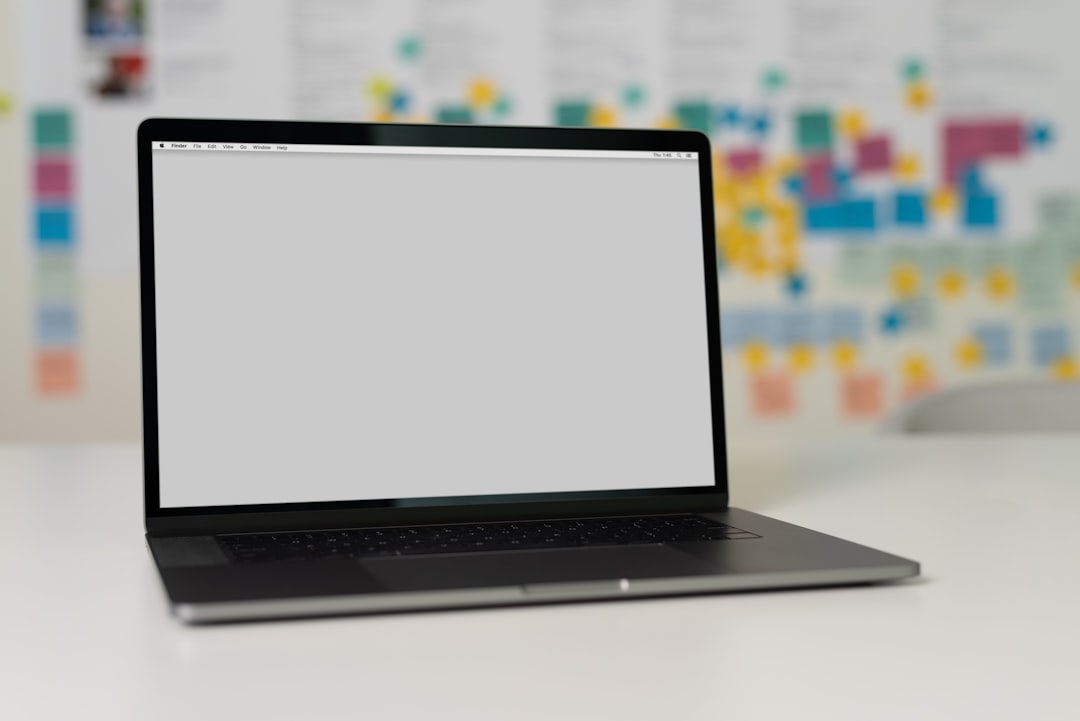 A laptop on a desk with a gray screen and colorful post-it notes in the background